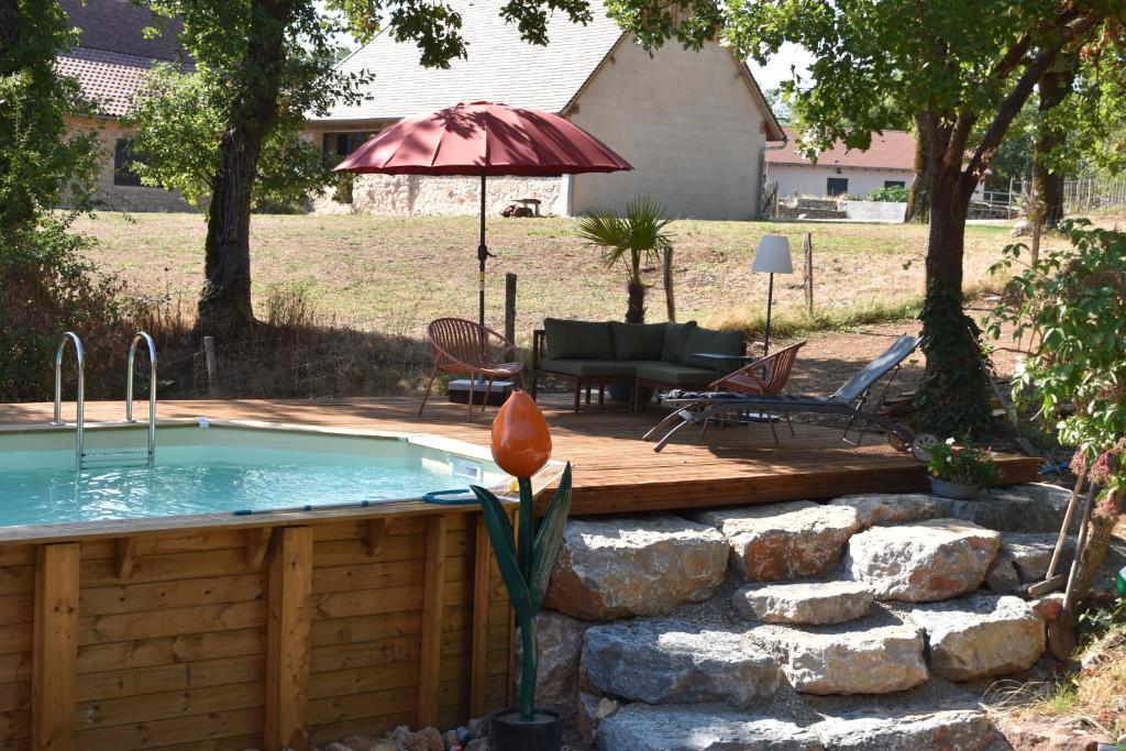 a swimming pool with a wooden deck and an umbrella at Trésor en Bois Chambres d'Hôtes in Autoire