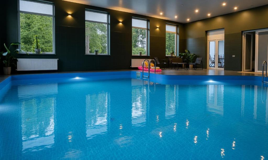 a large blue swimming pool in a room with windows at Lapsiņmuiža Pool House - Pool, Sauna & Hot-tub included in Dzedri