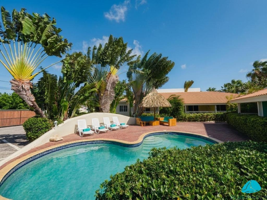 a swimming pool with chairs and palm trees at Blue Marlin Apartments, nabij Mambo Beach in Willemstad
