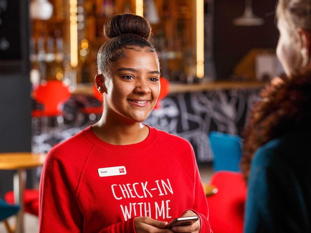 a young girl is smiling while holding a cell phone at ibis London Wembley in London