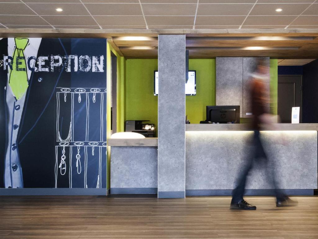 a person walking past a reception desk in an office at ibis budget Goussainville Charles de Gaulle in Goussainville