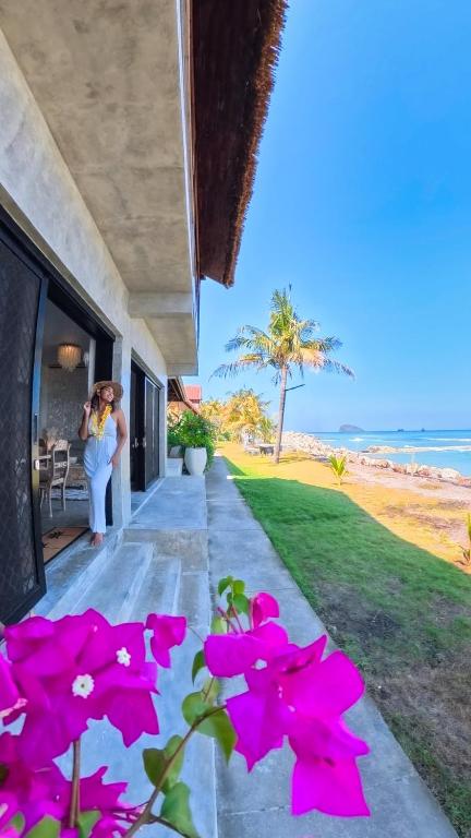 a woman standing on the porch of a house with pink flowers at Bali Secrets Oceanfront Villas in Candidasa