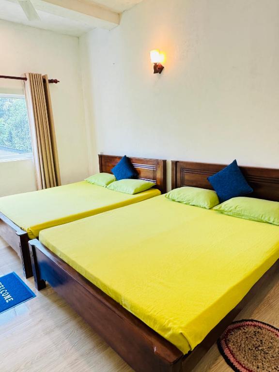 two beds in a room with yellow sheets and blue pillows at Nila Villa & Homestay in Galle