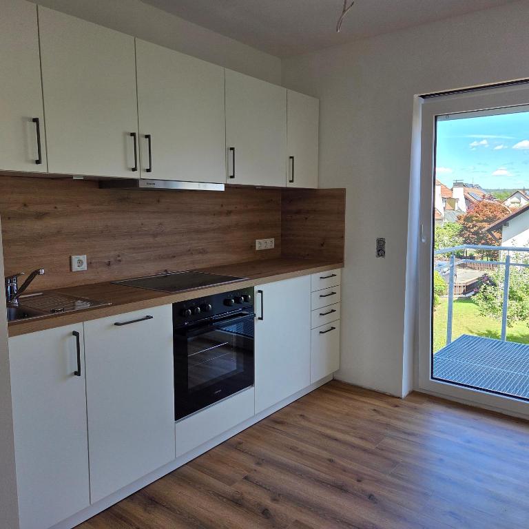 a kitchen with white cabinets and a large window at schöne Neubau Ferienwohnung "Wiesent" mit Küche und Balkon in Forchheim