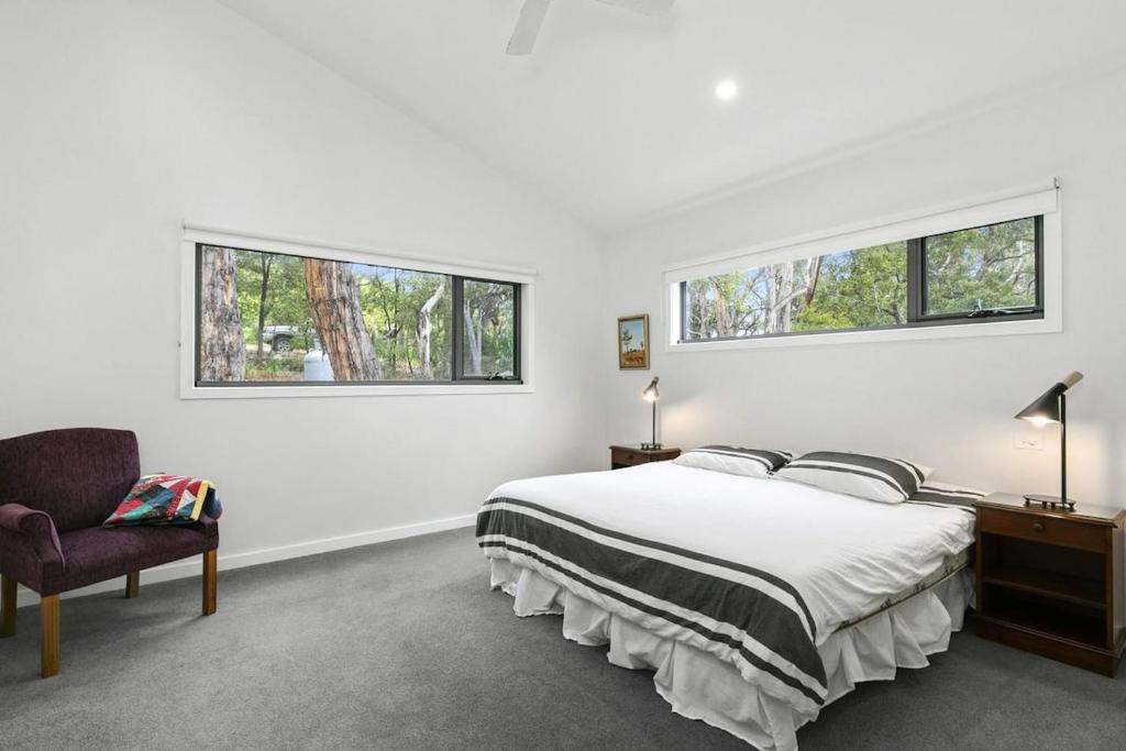 a white bedroom with a bed and two windows at Alto Vista in Lorne