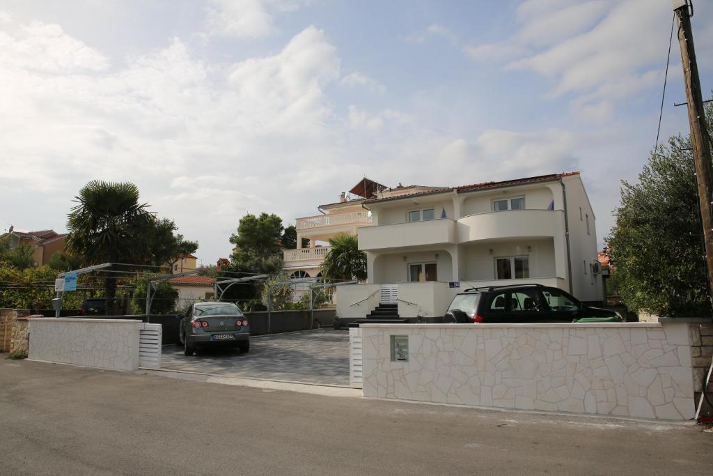 a white house with cars parked in a parking lot at Apartments Gabrijel in Vodice