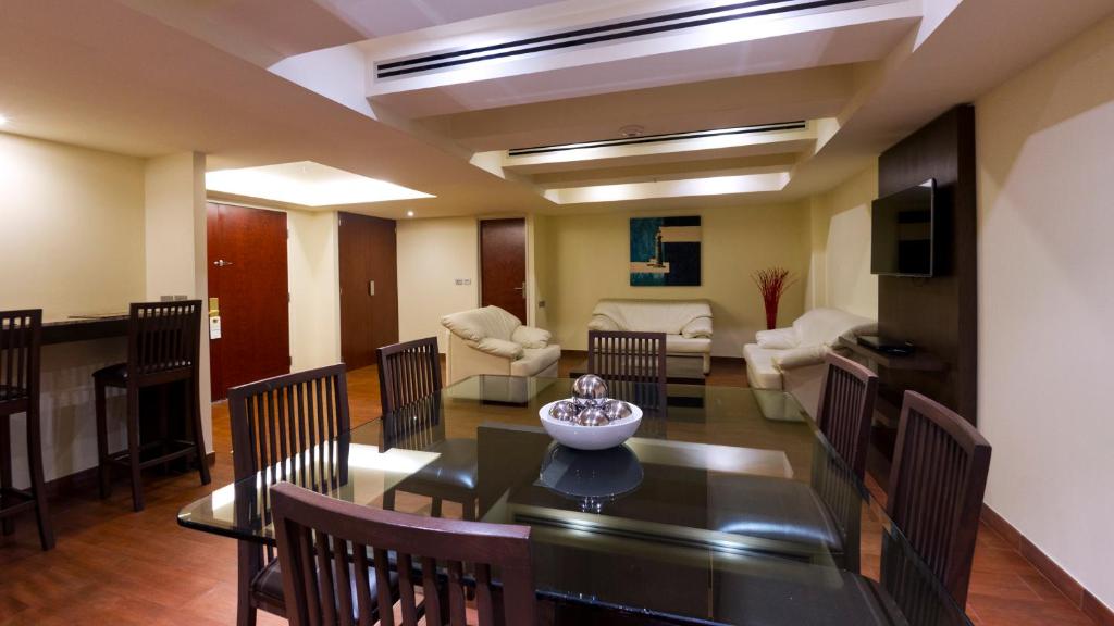 A combined lounge and dining area with a glass dining table, armchairs, and a wall-mounted TV.