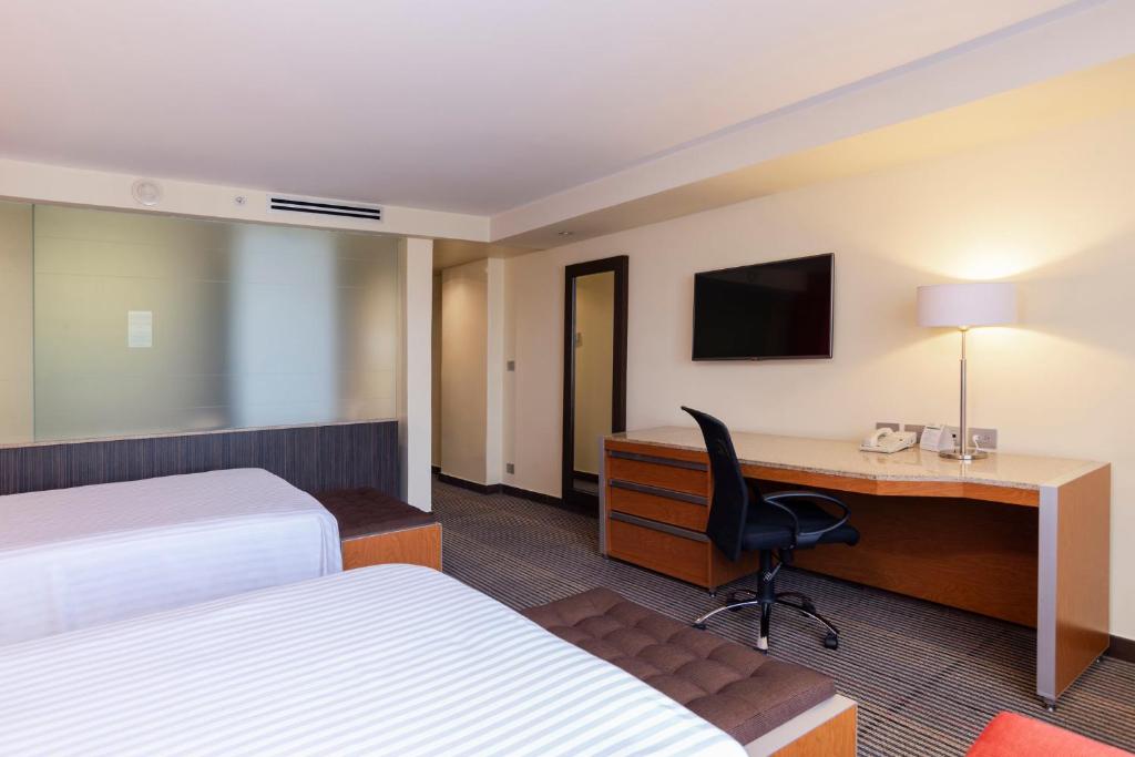 A two-bed room with a full-length desk, office chair, and wall-mounted television.
