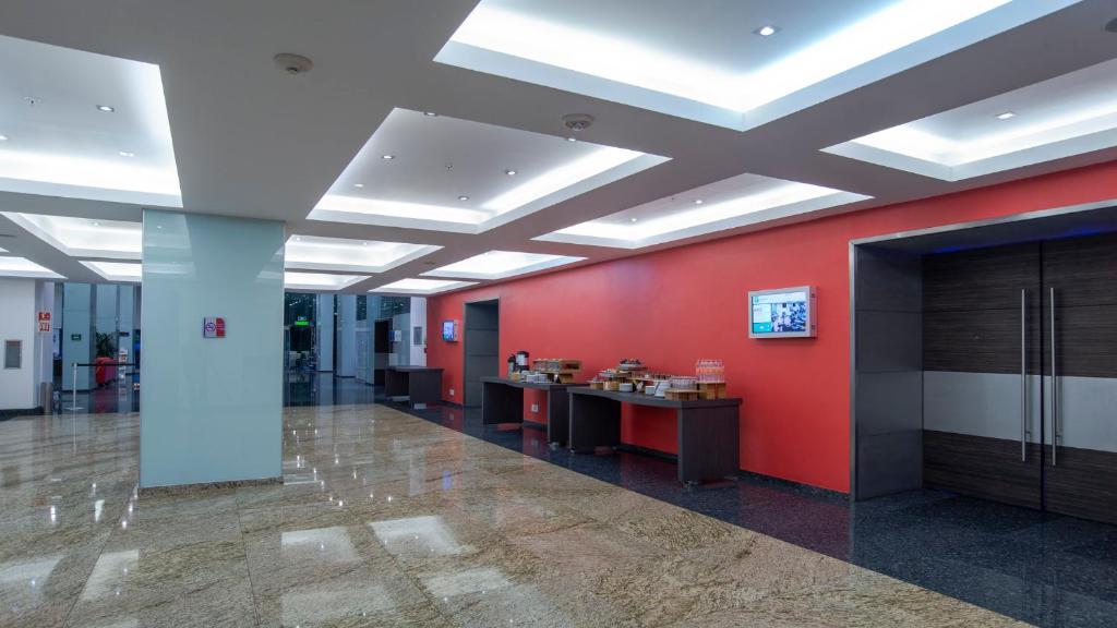 A bright lobby with red walls, reception desks and elevator doors.