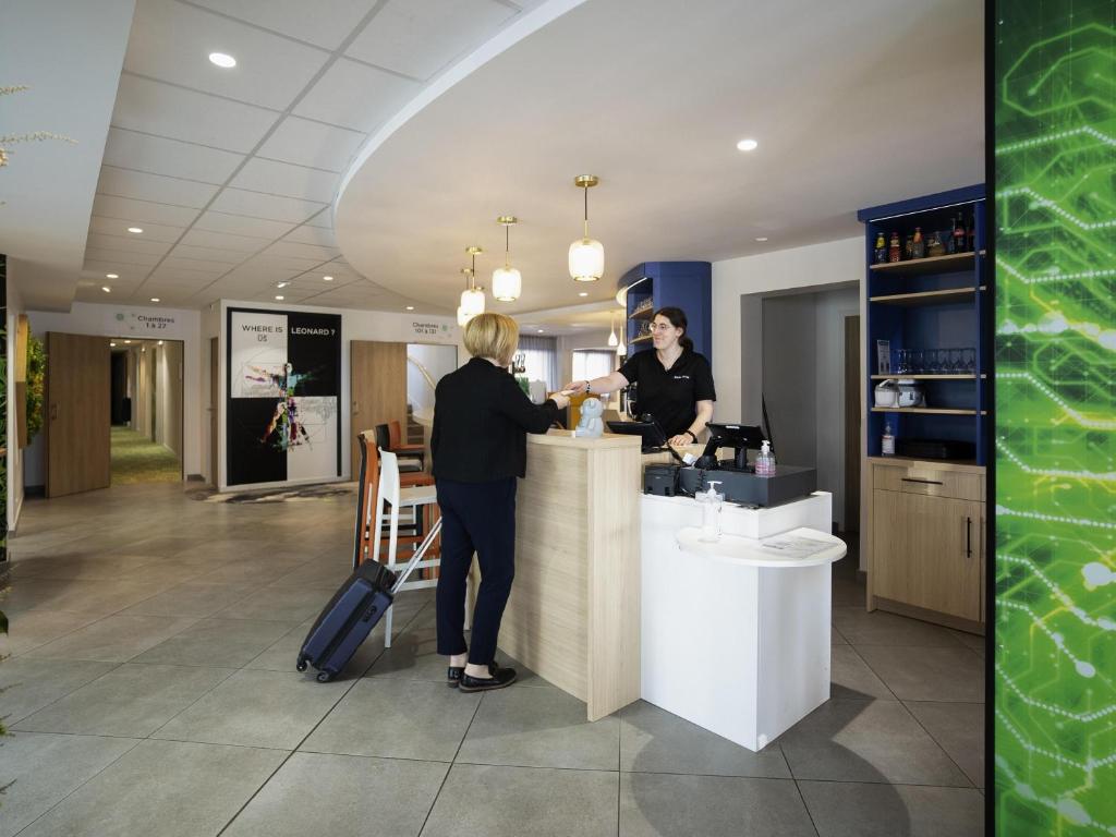 a woman is standing at a counter at a bar at ibis Styles Fougeres in Beaucé