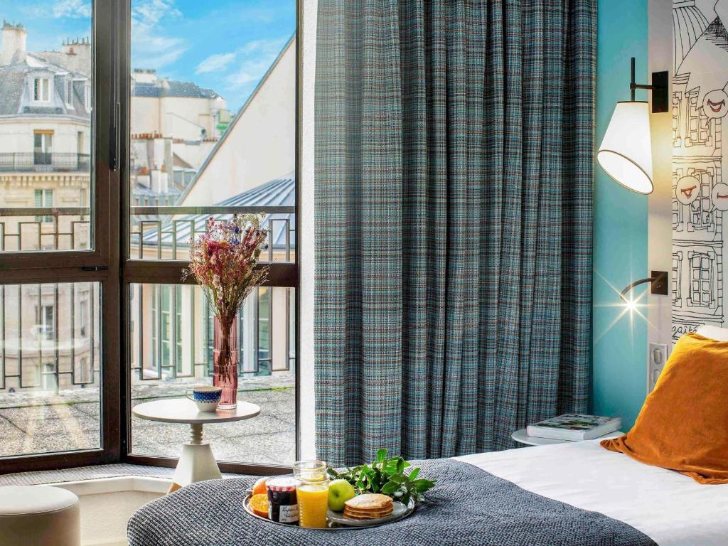 a room with a bed and a window with a tray of food at Mercure Paris Centre Gare Montparnasse in Paris