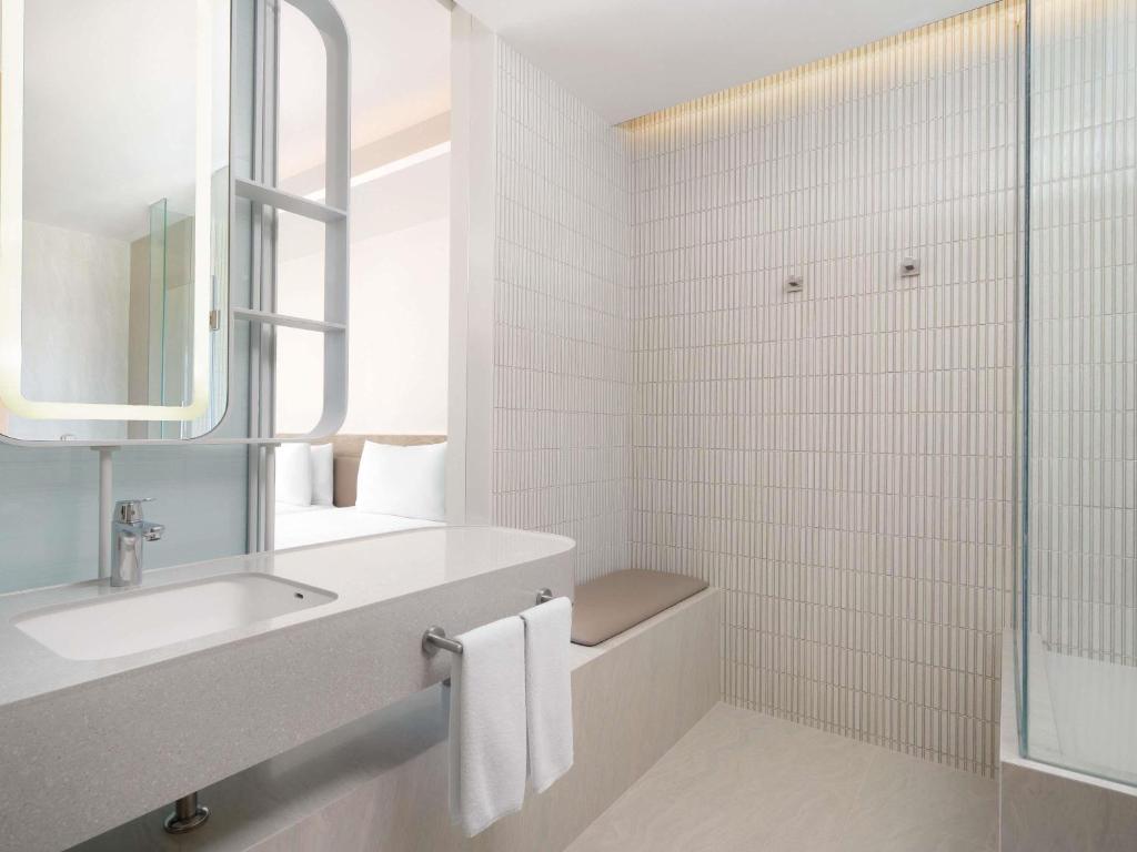 A bright white bathroom with a wide vanity, magnifying mirror, and glass-enclosed shower.