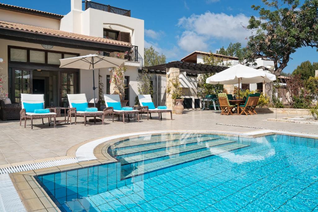 a swimming pool with chairs and umbrellas next to a house at 3 bedroom Villa Anassa with private pool and gardens, Aphrodite Hills Resort in Kouklia