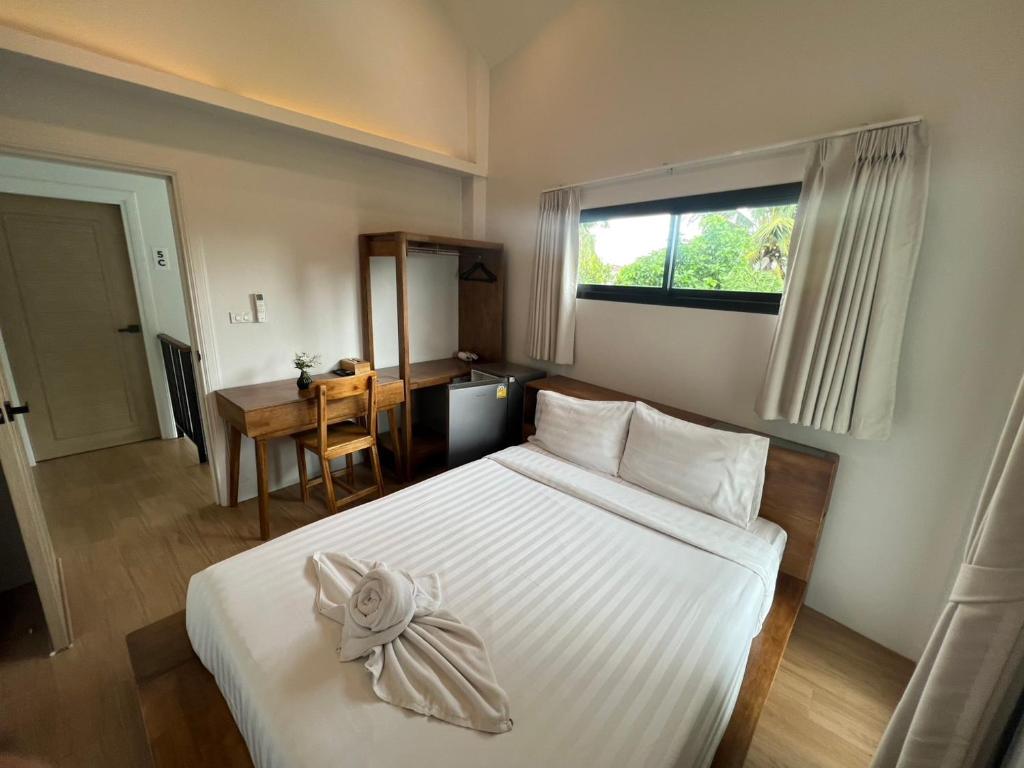 A bright double bedroom with a wooden desk, open wardrobe, minibar and curtained window.