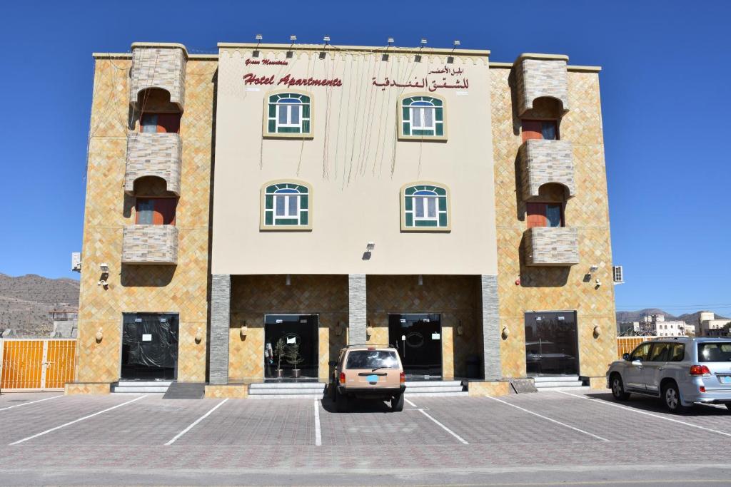 a building with cars parked in a parking lot at Green Mountain Hotel Apartments in Al ‘Aqar