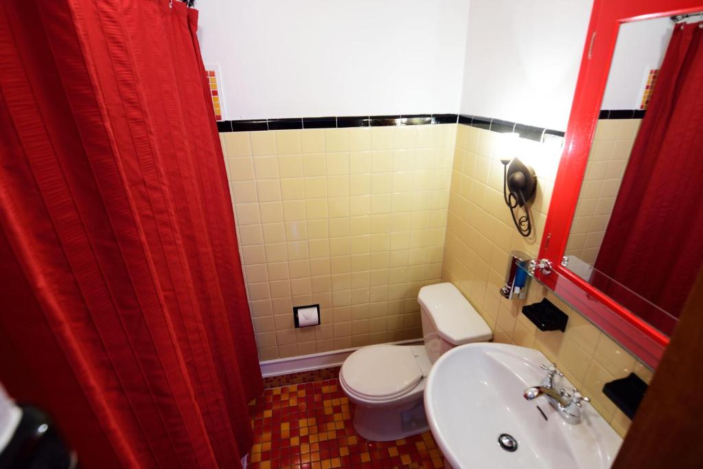 a bathroom with a toilet and a sink and a red shower curtain at Auberge le St-Georges in Saguenay