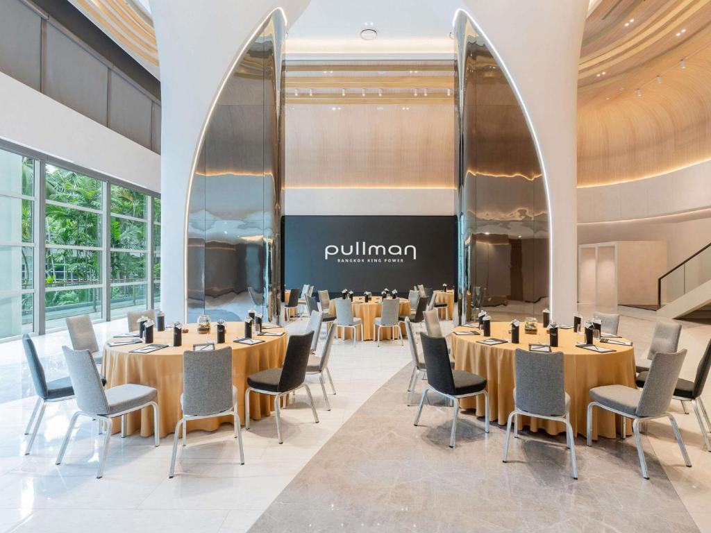 A bright event room with round banquet tables, flexible seating and tall windows overlooking greenery.