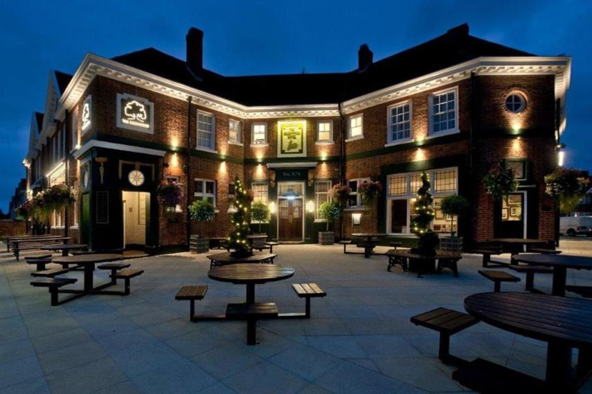 un grand bâtiment avec des tables et des bancs devant lui dans l'établissement The Greenwood Hotel - Wetherspoon, à Northolt