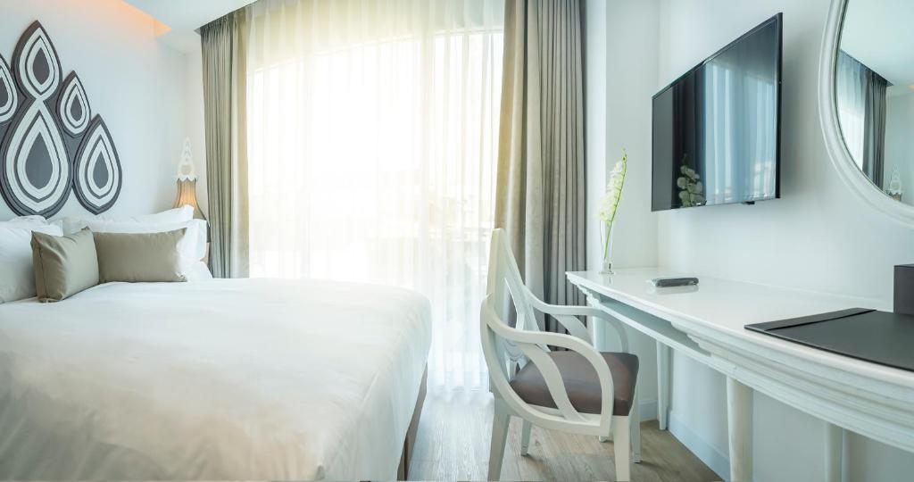 A bedroom work area beside the bed, with a desk, chair, television, and bright curtained window.