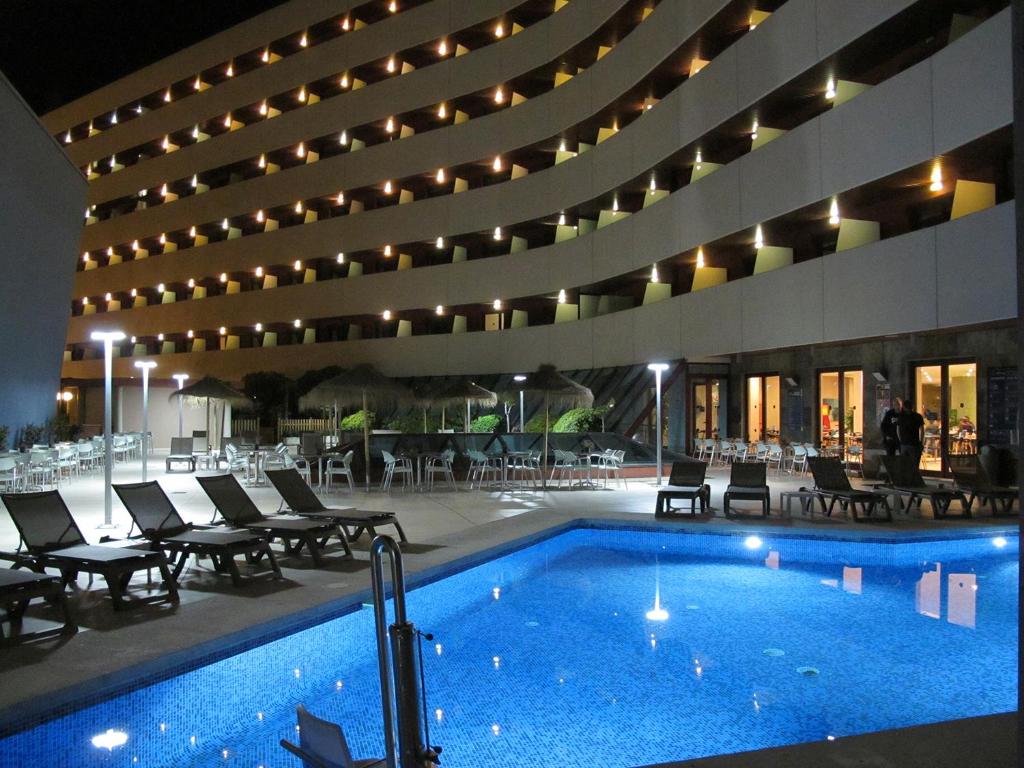 a hotel with a swimming pool and chairs and a building at Ohtels Campo De Gibraltar in La Línea de la Concepción