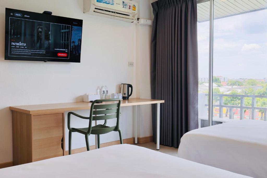 A guest room with a narrow desk, smart TV, kettle and balcony-facing window.