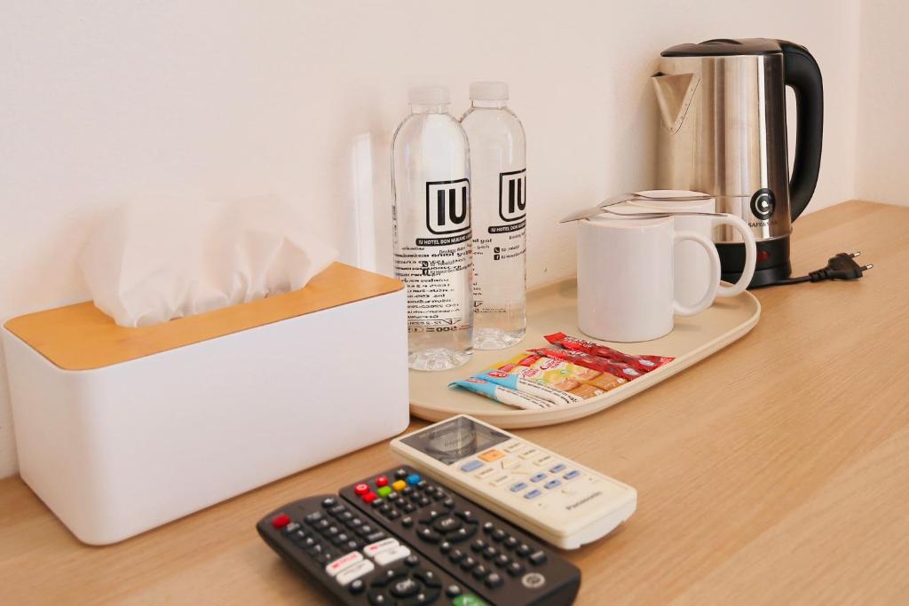 A room refreshment station with bottled water, an electric kettle, cups, tea supplies, tissues, and remotes.