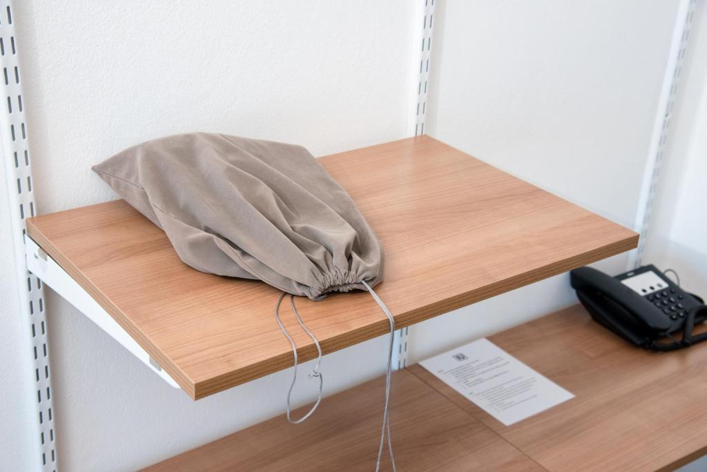 A small wooden shelving unit with a fabric bag and a room telephone.