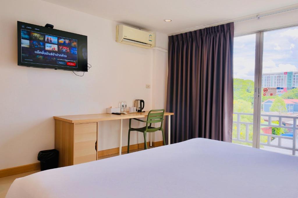 A double bed faces a compact desk, wall-mounted TV, air conditioner, and glazed balcony door.