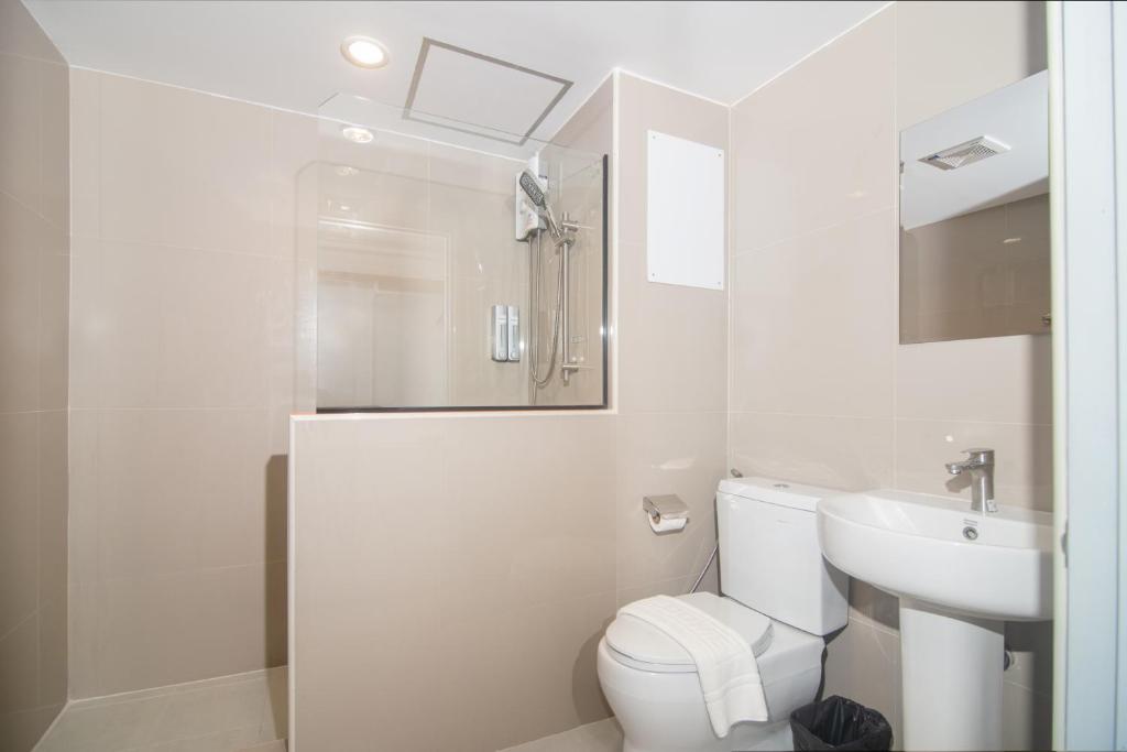 A compact tiled bathroom with a toilet, pedestal sink, and enclosed shower area.