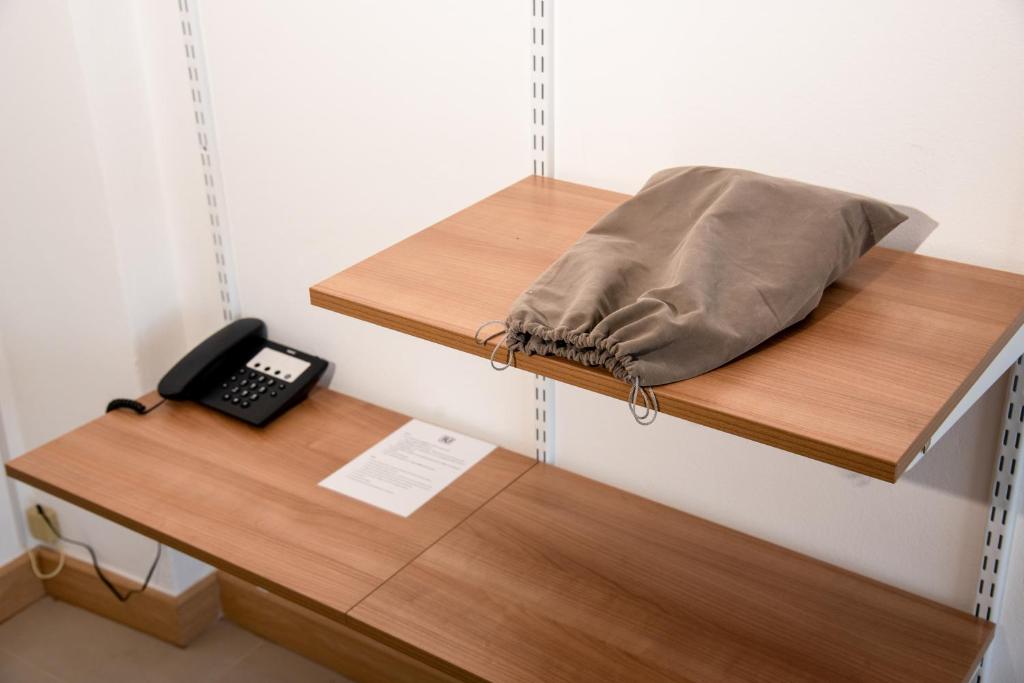 A compact wood desk includes a telephone, paperwork, and a raised shelf with a folded cushion or pillow.