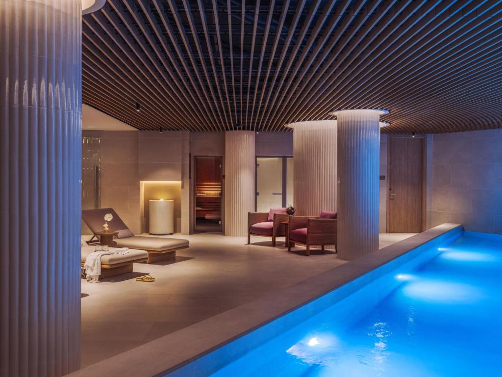An indoor pool sits beside a warmly furnished spa-like relaxation area under a dramatic slatted ceiling.