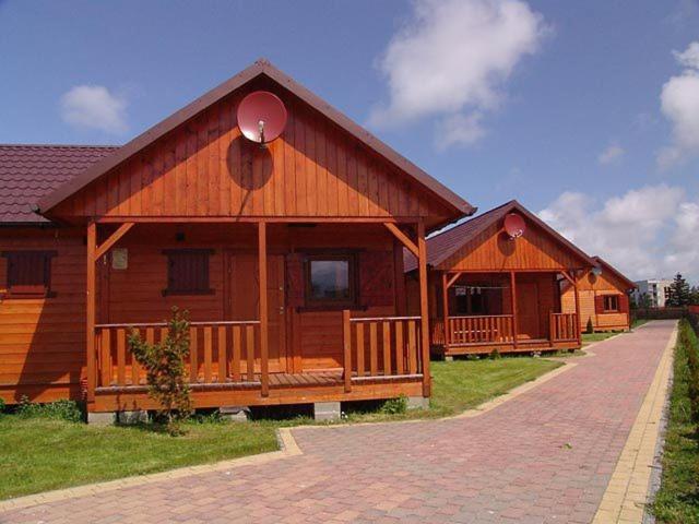 a large wooden cabin with a porch on a field at Domki Letniskowe Pikamar in Darłówko