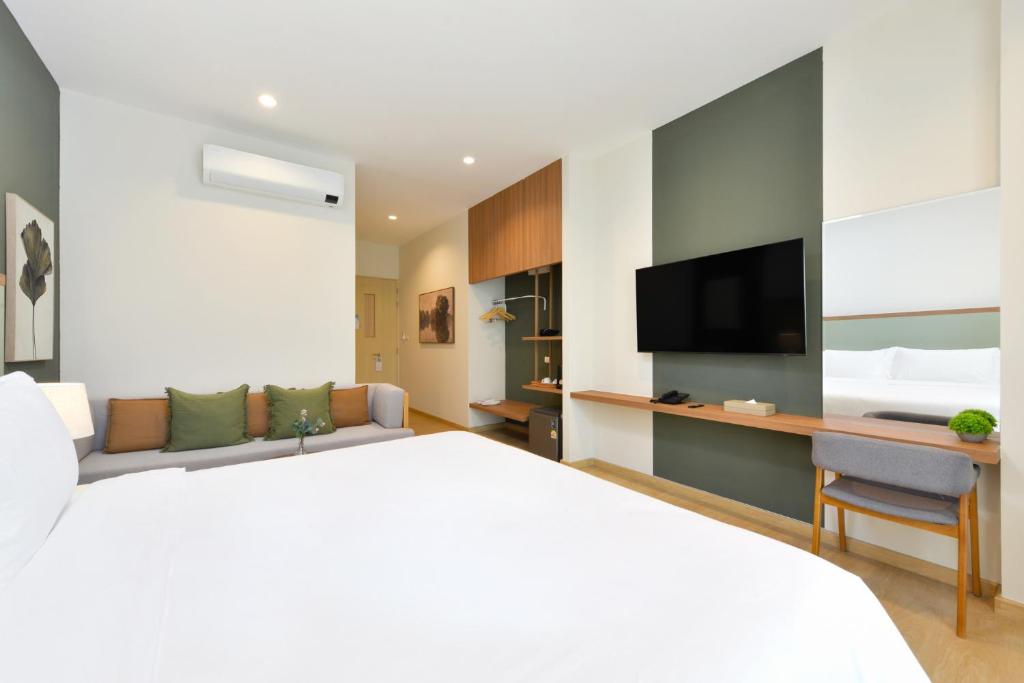 A guest room viewed from the bed toward the television, desk, sofa, and entry area.