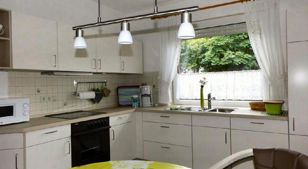 eine Küche mit weißen Schränken, einem Waschbecken und einem Fenster in der Unterkunft Ferienwohnungen Akzent in Papenburg