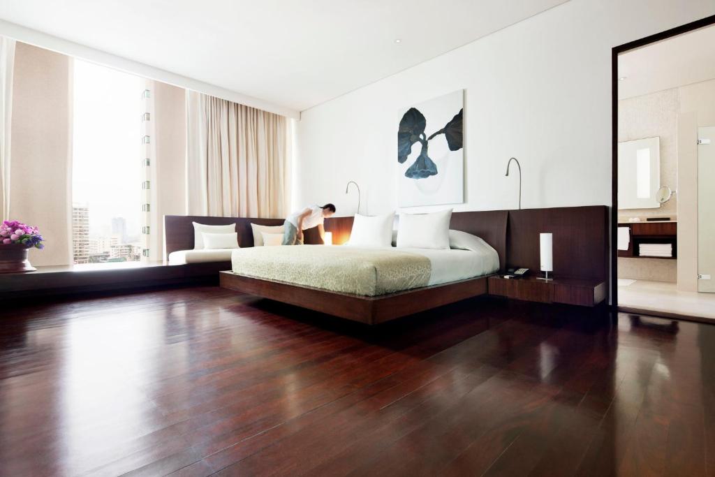 A spacious bedroom with a large bed, polished wood floor and a bright urban window.