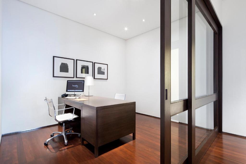 A private office with a dark wood desk, computer and rolling chair behind glass-panel doors.
