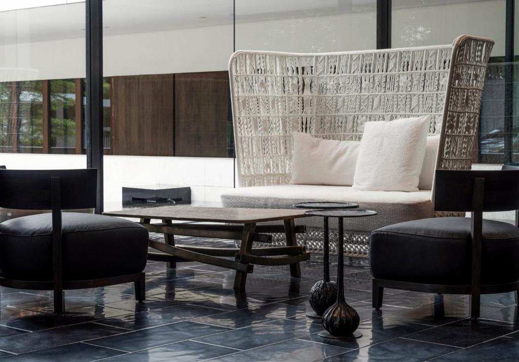 A bright lounge with a woven sofa, two dark armchairs and low coffee tables.