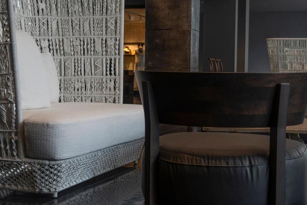 A dark round table and leather chair sit beside a woven upholstered lounge chair.