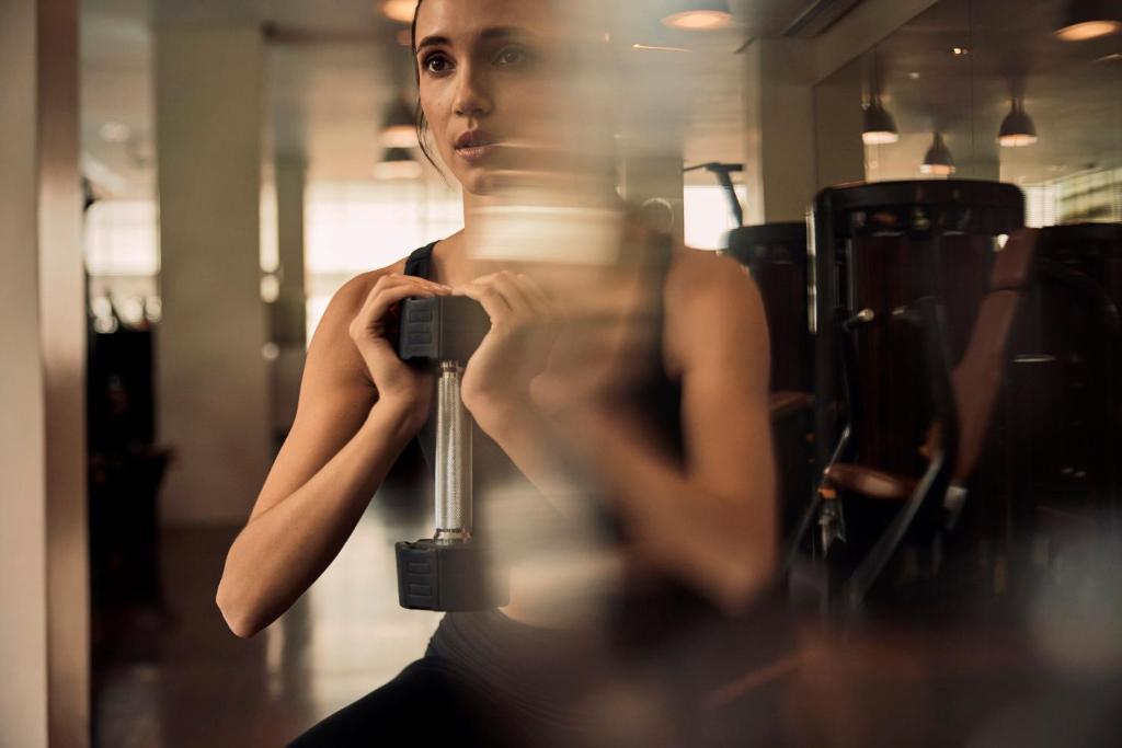 A close gym portrait shows a woman holding a dumbbell in front of a mirrored wall.