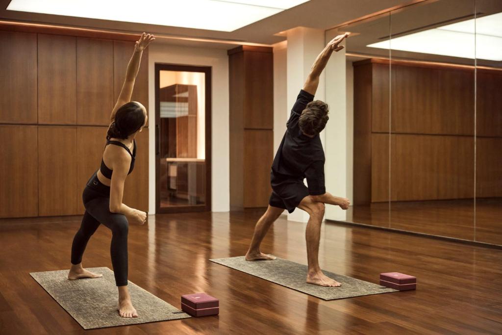 Two guests practise yoga in a wood-floored mirrored studio.
