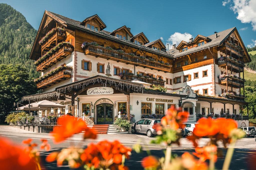 a large building with orange flowers in front of it at Kristallhotel Corona-Krone in San Vigilio Di Marebbe