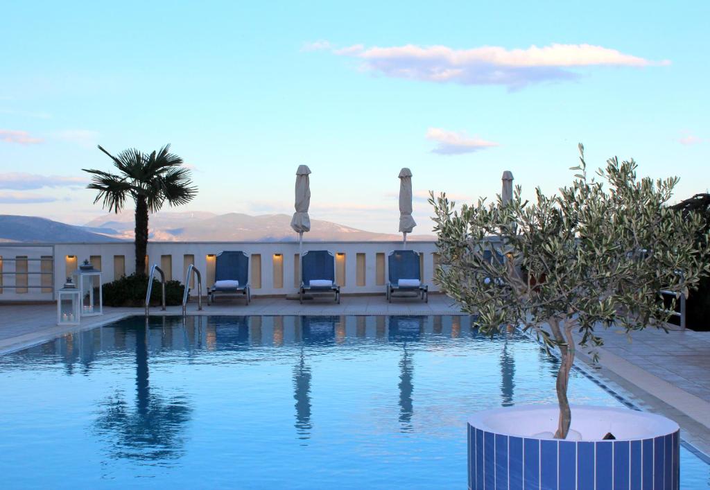 a swimming pool with chairs and trees in front of a building at Amaryllis Hotel Apartments in Tolo