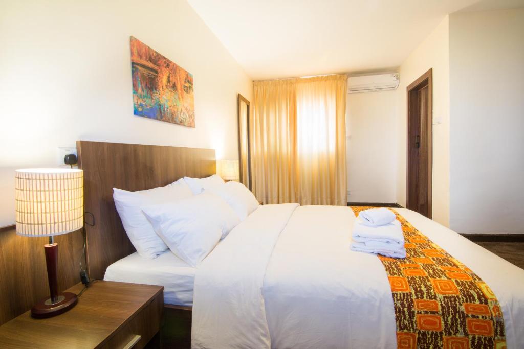 um quarto com uma grande cama branca e um candeeiro em Sinclair Guest House em Abuja