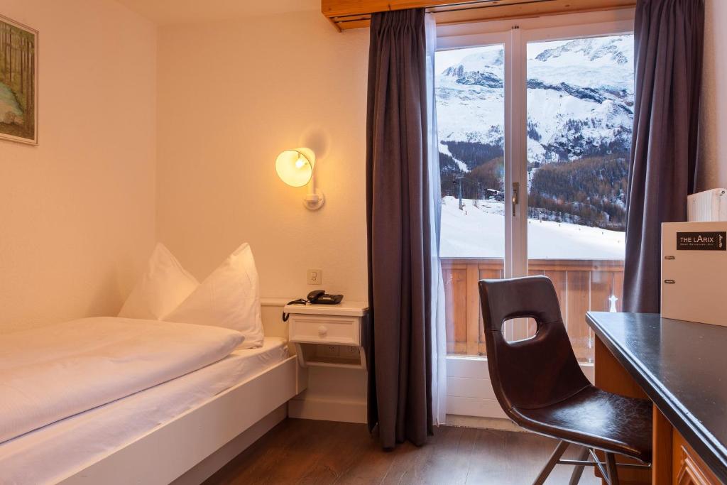 a bedroom with a bed and a desk and a window at Hotel THE LARIX ski-in ski-out in Saas-Fee