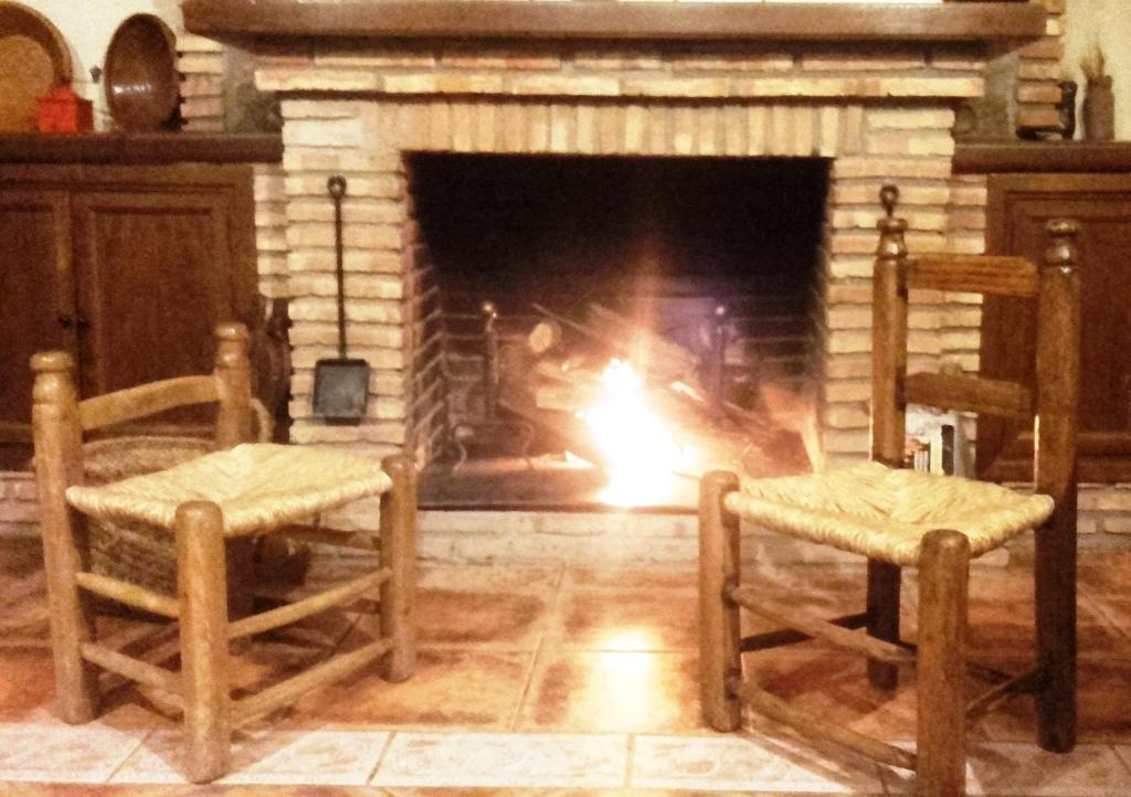 a fireplace with two chairs in front of it with a fire at Casa Rural Peña Falcón in Torrejón el Rubio