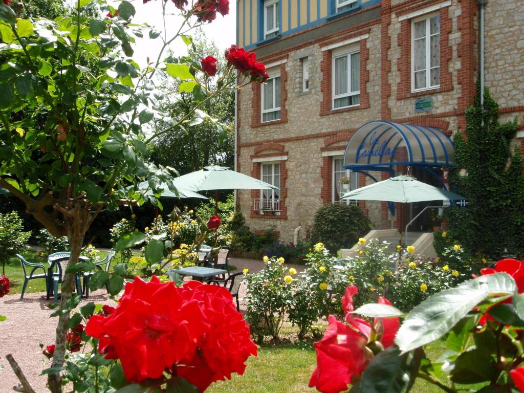 un jardín con rosas rojas y sombrillas frente a un edificio en Les Camelias, en Bagnoles de l'Orne