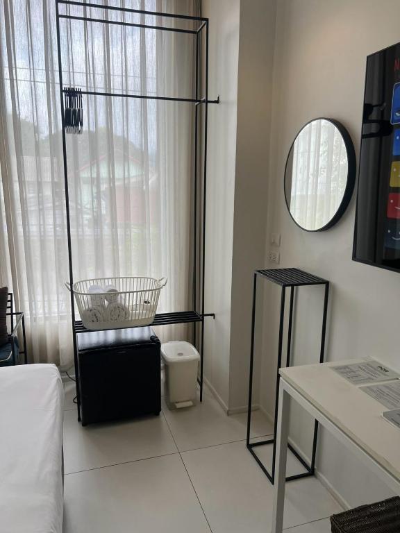 A view across the bed area toward the open clothes rack, window and desk.
