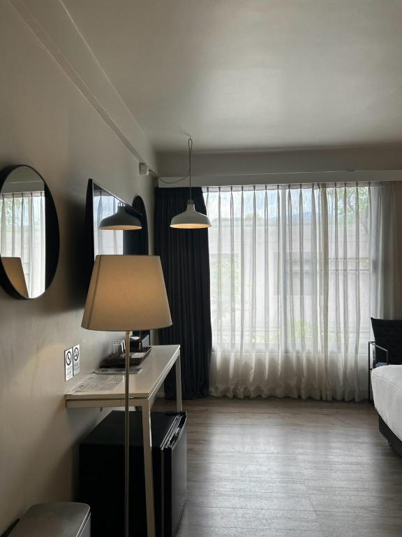 A slim in-room desk beside a large curtained window, with a lamp, mirror and television.