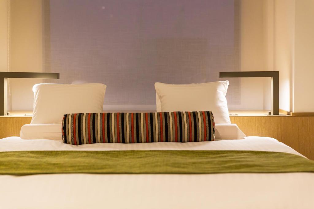a bed with white sheets and pillows with a green blanket at HOTEL MYSTAYS PREMIER Omori in Tokyo