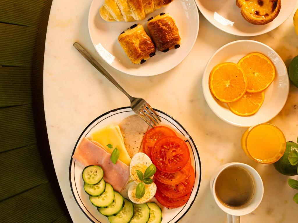 A breakfast table with pastries, cold cuts, fruit, juice and coffee.